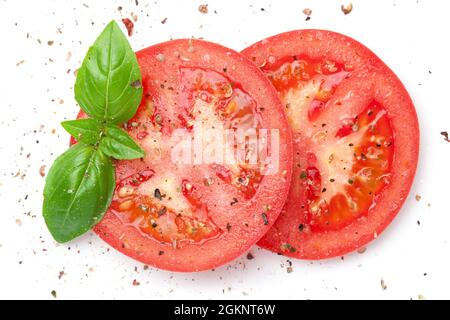 Pomodori rossi a fette cosparsi di pepe appena macinato con foglie di basilico verde isolato su sfondo bianco. Vista dall'alto, disposizione piatta Foto Stock