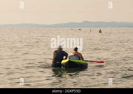Due uomini di mezza età in riva al mare con una canoa con la costa toscana sullo sfondo al tramonto, Marina di Castagneto Carducci, Livorno, Toscana Foto Stock
