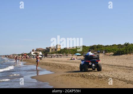 Poliziotto in quad pattugliando la spiaggia sabbiosa con gente che gode il mare in estate, Marina di Castagneto Carducci, Livorno, Toscana, Italia Foto Stock