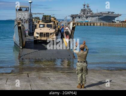 WHITE BEACH, Giappone (Jun. 10, 2021) Seaman Marla Sandoval, di Des Moines, Ia. e assegnato alla Naval Beach Unit 7, lavora con il personale di servizio dell'imbarcazione di atterraggio per dirigere un veicolo tattico leggero congiunto della III Marine Expeditionary Force sulla LCU presso la Comandante, attività della flotta Okinawa White Beach Naval Facility, Okinawa, Giappone Jun. 10, 2021. Nave d'assalto anfibio di classe americana USS America (LHA 6) è ormeggiata lato molo sullo sfondo. Foto Stock