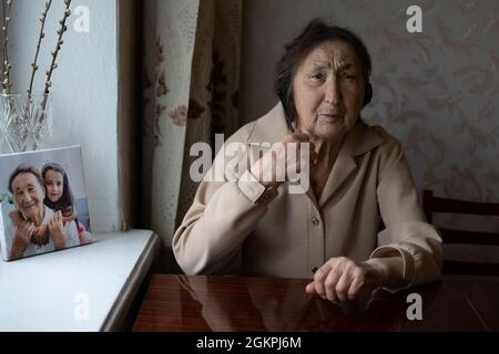 donna molto anziana in cuffia che fa la conversazione video sul telefono nella loro casa. Concetto di conversazione video. Headshot online. Foto Stock