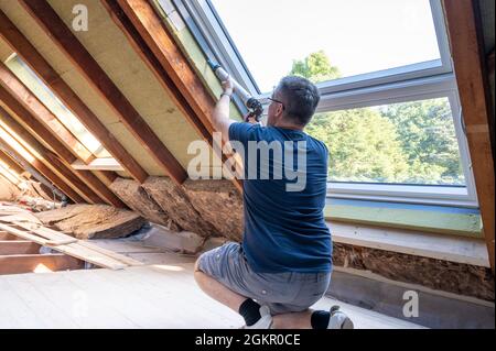 Artigiano che caulking una nuova finestra in soffitta. Foto Stock