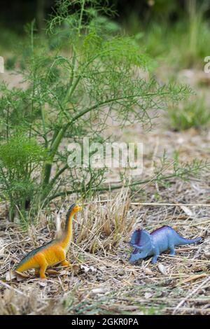 Scatto verticale di due piccoli giocattoli colorati di dinosauro di plastica sul terreno all'aperto Foto Stock