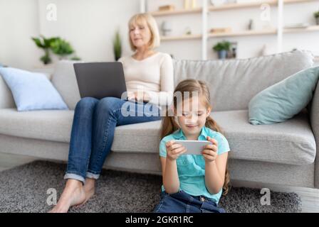 Donna matura e nipote che utilizzano il computer portatile e il telefono cellulare Foto Stock