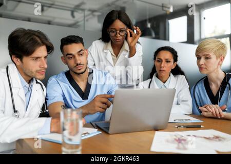 Gruppo multietnico concentrato di medici seduti al tavolo, utilizzando un computer portatile Foto Stock