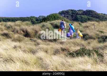 La famiglia cammina sul sentiero attraverso le dune di sabbia fino al mare in una calda giornata di sole a West Wittering, Chichester Harbour, West Sussex, Inghilterra Foto Stock