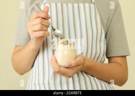 Donna in grembiule tiene il cucchiaio e il vasetto di vetro con yogurt alla pesca Foto Stock