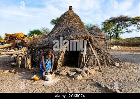 Donna che macina Sorghum di fronte ad una capanna tradizionale della tribù Toposa, Equatoria Orientale, Sudan del Sud, Africa Foto Stock