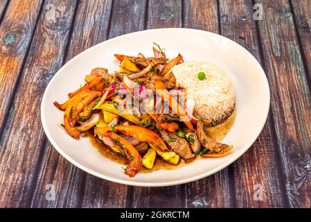 Ricetta tipica di un ristorante peruviano di sirloin saltato con verdure, patatine fritte, riso bianco e salsa di soia con un sacco di punch Foto Stock