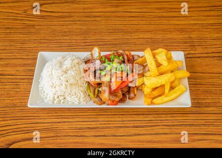 Piatto di ricetta tipica dal Perù con lomo saltado, patatine fatte in casa e riso bianco su tavola di legno Foto Stock