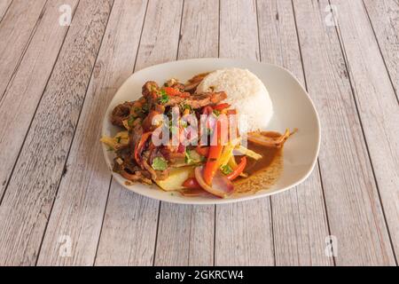 Piatto pieno di tipica ricetta peruviana lomo saltado accompagnato da riso, peperoni e cipolla rossa e patatine fatte in casa su un tavolo di legno chiaro Foto Stock