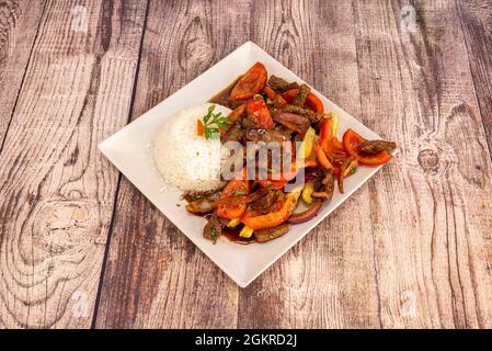 Fantastica ricetta tradizionale peruviana lomo saltado con porzione di riso bianco, pezzi di filetto, pomodori e peperoni saltati con salsa di soia Frenc Foto Stock