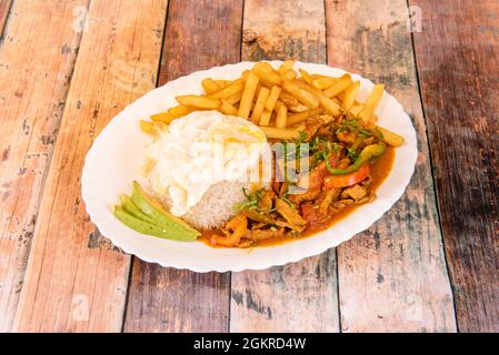 Lomo saltado peruviano con verdure, salsa, uova e patatine, riso e un po' di avocado su un piatto bianco Foto Stock