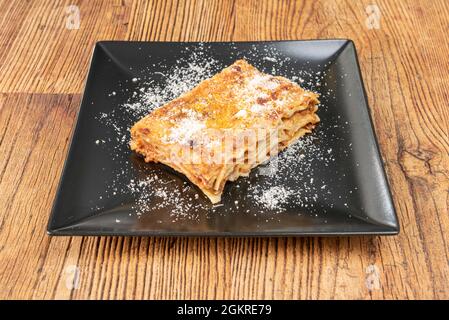 Ricetta di lasagna allo stufato di maiale con un sacco di formaggio, molti strati di gambe e un sacco di pomodoro su un piatto quadrato nero Foto Stock