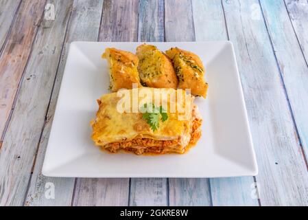 porzione di lasagna di pollo con i suoi strati di pasta, la parte superiore del gratin besciamella e un po' di pane all'aglio come un lato Foto Stock