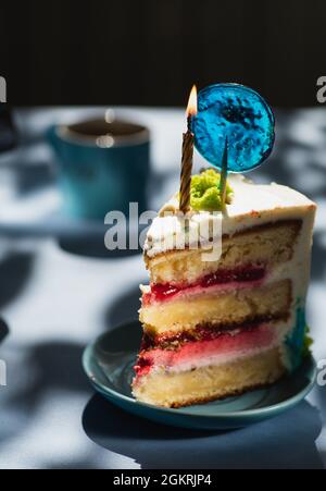 Piatto con fetta di gustosa torta fatta in casa sul tavolo, torta al lampone. Colourful lollipop swirl su bastone di legno. Candela che brucia sulla torta Foto Stock