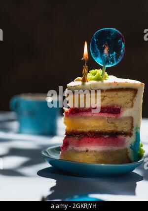 Piatto con fetta di gustosa torta fatta in casa sul tavolo, torta al lampone. Colourful lollipop swirl su bastone di legno. Candela che brucia sulla torta Foto Stock