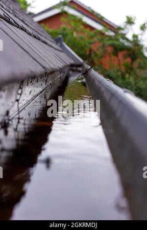 Un ritratto di una grondaia del tetto ostruita piena di acqua piovana durante una giornata piovosa e nuvolosa. Il fondo dello scarico è pieno di foglie e di altra wast naturale Foto Stock