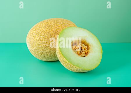 Meloni di Gallia maturi. Un melone si divide a metà mostrando i suoi semi su uno sfondo verde semplice Foto Stock