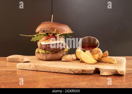 Hamburger di manzo in stile messicano con guacamole, rucola, formaggio di capra e un lato di patatine fritte deluxe Foto Stock