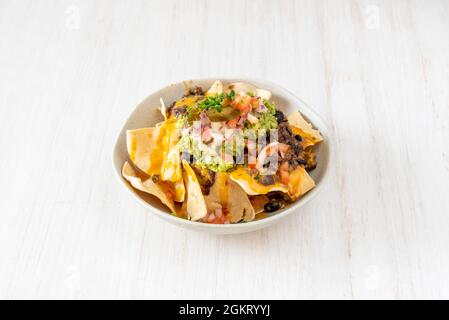 ciotola di nacho juarez con guacamole, cipolla tritata, fagioli al peperoncino, nachos di grano e erba cipollina tritata Foto Stock