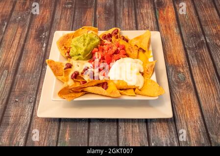 Contadini nachos con guacamole, Pico de gallo, fagioli rossi e due tipi di formaggio su stoviglie bianche Foto Stock