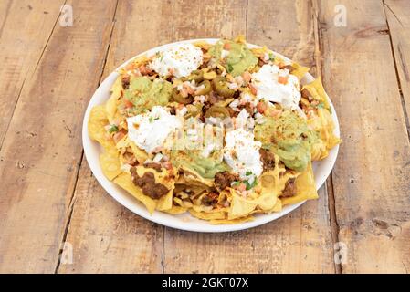 Piatto traboccante di nachos di mais messicano con guacamole, formaggio cremoso, cipolla bianca tritata, pomodoro julienne, chili con carne e jalapenos Foto Stock