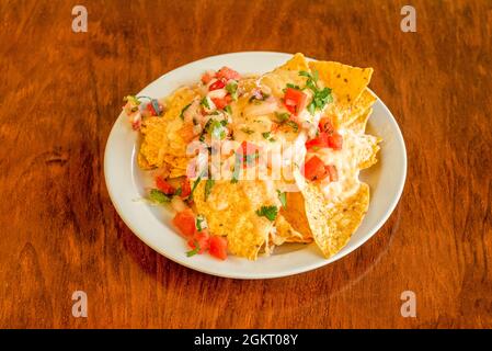 Mais nachos con Pico de gallo, prezzemolo e coriandolo e formaggio fuso su piatto bianco e tavola di legno Foto Stock