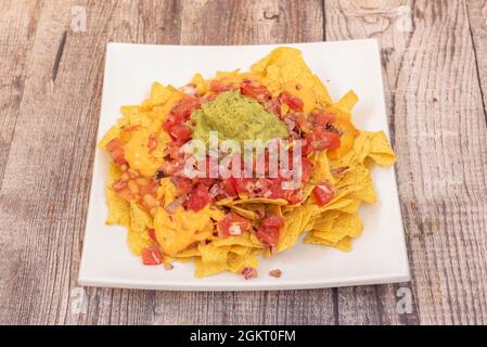 Piatto di nachos con guacamole, formaggio cheddar, pomodoro tritato e cipolla con fagioli in salsa Foto Stock