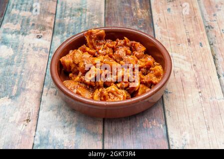 Tapa spagnola di orecchio di maiale marinato all'interno di una padella di argilla su un tavolo di legno Foto Stock