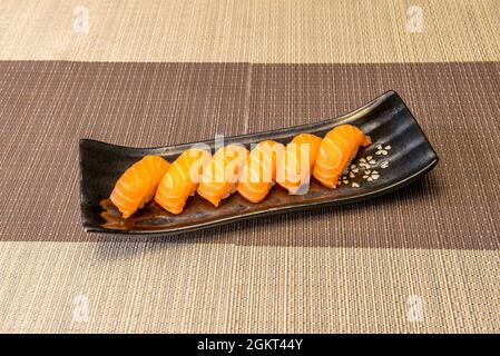 Sei porzioni di super appetitoso sushi nigiri di salmone norvegese su vassoio di porcellana nera con motivi floreali asiatici Foto Stock
