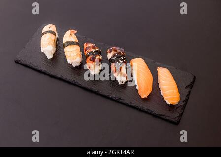 Vassoio di tre sushi di nigiri con salmone norvegese, anguilla fluviale e gamberi di Huelva su piatto di ardesia nera Foto Stock