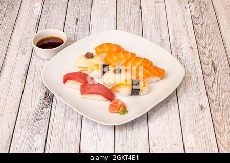 Piatto con sushi di nigiri salmone assortito, gamberi su riso, tonno rosso, pesce farfalla con uova di pesce con wasabi e ginseng con ciotola con salsa di soia Foto Stock