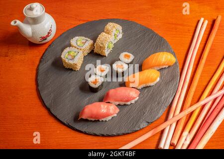 Sushi assortito su un piatto circolare nero ardesia e barca salsa con salsa di soia. Makis di salmone, nigiri di tonno e salmone, uramaki con semi di sesamo e avoc Foto Stock