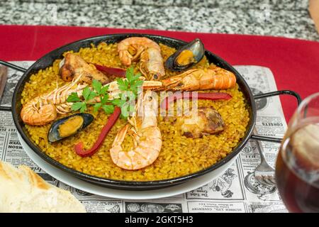 Grande paella estiva spagnola mista per due con pollo stufato e gamberi, gamberi e gamberi, gamberi e cozze, un po' di pepe rosso e zafferano su un tavolo in una re turistica Foto Stock