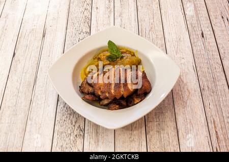 Deliziosa anatra arrosto guarnita con melanzane tostate e foglie di menta su un piatto bianco profondo Foto Stock