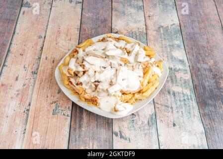 Abbondante porzione di patate fritte con pollo stufato e salsa di cesar su tavola di legno Foto Stock