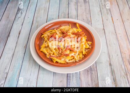 Piatto di argilla con patatine fritte e strisce di pancetta con formaggio grattugiato fuso su tavola di legno Foto Stock