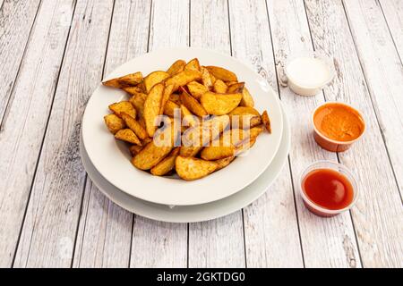 Una grande porzione di patatine fritte tagliate a spicchi con salse assortite da condire Foto Stock