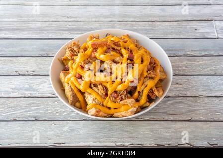 grande ciotola di pollo fritto e patate con pancetta condita con un sacco di formaggio cheddar sulla parte superiore del tavolo di legno Foto Stock