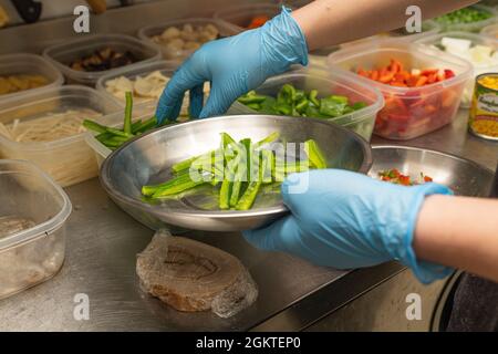 Mani di uno chef cinese che raccoglie gli ingredienti per preparare una ricetta di cucina asiatica Foto Stock