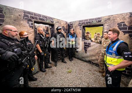 Il sergente Wayne Dowson del Dipartimento di polizia del Northamptonshire, a destra, responsabile della formazione della polizia armata, parla con gli ufficiali di polizia della NHPD e degli Airmen della 422nd Security Forces Squadron dopo un'esercitazione attiva di risposta dello sparatutto di tre agenzie alla RAF Croughton, Inghilterra, 30 giugno 2021. Gli airman del 422° SFS, insieme agli ufficiali della polizia della NHPD e del Ministero della Difesa, hanno partecipato a molteplici esercizi per migliorare le loro tattiche di ricerca e sequestro, rafforzare i legami locali e ottenere rapporti con i loro compagni di polizia. Foto Stock