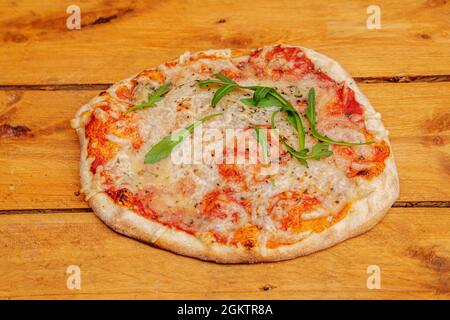 Piccola pizza margarita con un sacco di formaggio e pomodoro e alcune foglie di rucola da decorare su tavola di legno Foto Stock