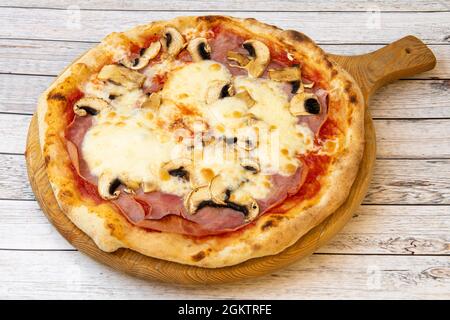 Fantastica pizza alla crosta sottile con prosciutto, funghi e mozzarella al gratin su tavola di legno Foto Stock