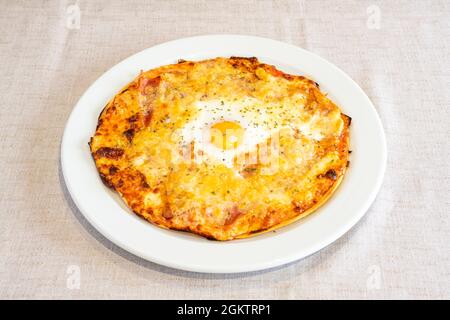 Pizza rustica italiana con un sacco di formaggio gratinato e un uovo fritto al centro su un piatto bianco Foto Stock