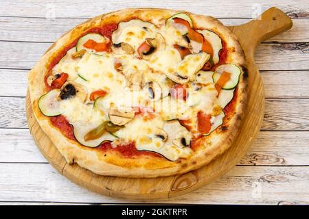 Spettacolare pizza vegetariana con crosta sottile, funghi, peperoni e zucchine su tavola di legno non verniciata Foto Stock