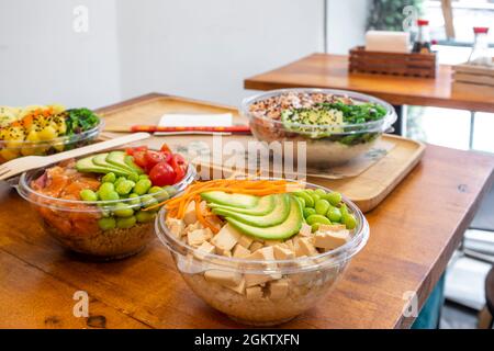 Ciotola di poke con tofu a dadini, fagioli di edamame, fette di avocado, riso bianco base e un contenitore da servire a casa mentre aspettate su un tavolo da ristorante Foto Stock