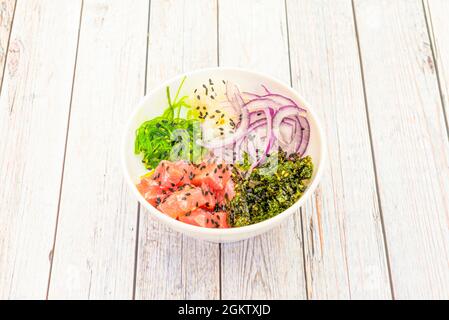 Ciotola di poke di tonno rosso hawaiano con cipolla rossa in anelli, insalata di alghe di wakame, semi di sesamo e papavero su tavola bianca di legno Foto Stock