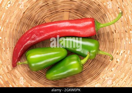 Tre cialde di pepe verde caldo e una rossa in un piatto di paglia, primo piano, vista dall'alto. Foto Stock