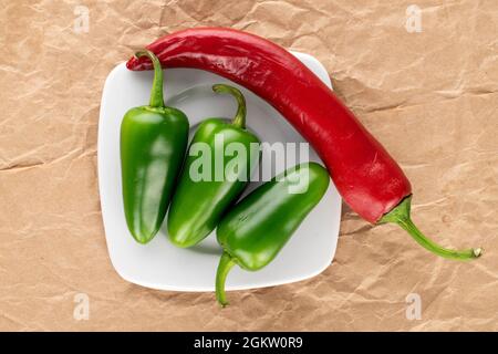 Tre cialde di peperoncino verde e una rossa con un piattino bianco su carta artigianale, primo piano, vista dall'alto. Foto Stock